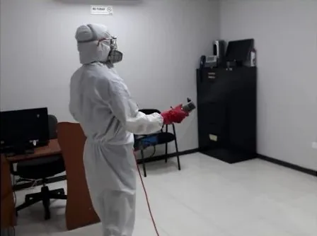 Técnico de ATRAPA-ME con equipo de protección aplicando tratamiento contra plagas en una oficina